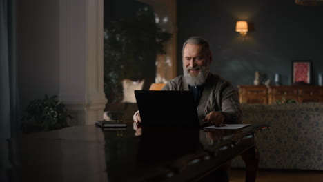 Happy-old-man-having-video-call-through-laptop-in-luxury-interior