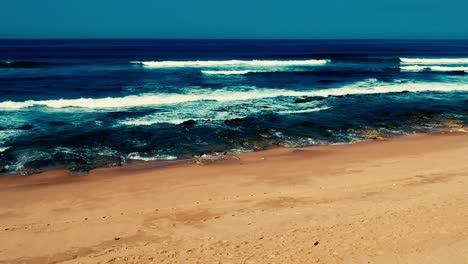 Aerial-footage-filmed-with-a-drone-overlooking-the-beach-and-sea-of-crashing-waves-with-a-deep-blue-ocean-on-the-Bluff-in-Africa-southern-hemisphere