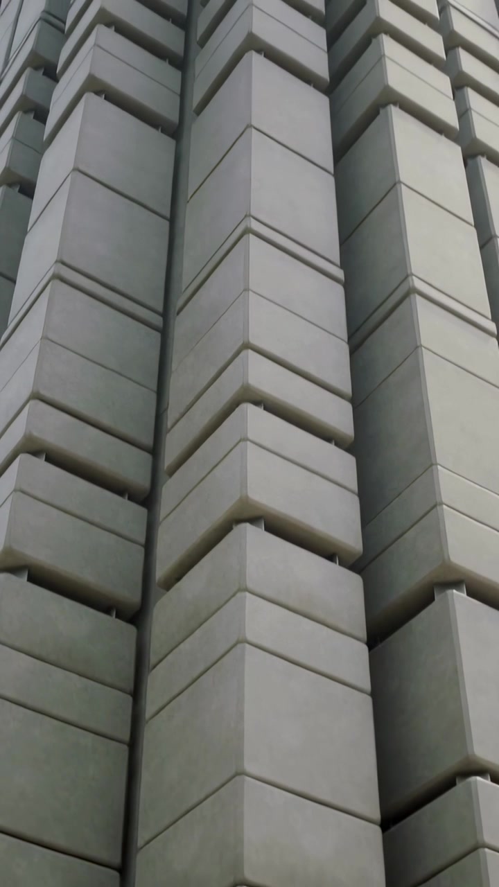 Vídeo vertical: Câmera inclinando mostrando módulos de concreto empilhados ao nível da rua, juntas estreitas, céu