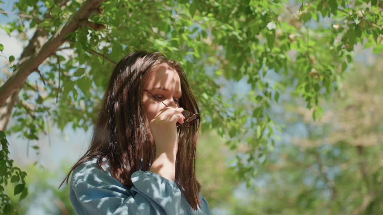 공원 분위기 속에서 햇빛을 즐기는 행복한 여성, 햇빛이 비치는 자연 속에서 머리카락을 휘날리며 즐거워하는 여성, 무성한 공원 풍경 속에서 햇빛을 쬐며 바람에 흩날리는 머리카락을 가진 쾌활한 여성