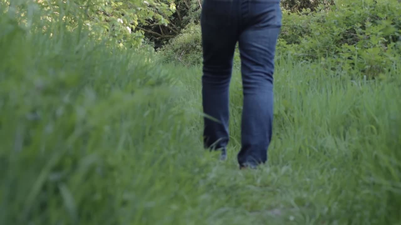 Woman walking through lush green meadow pathway wide tilting shot
