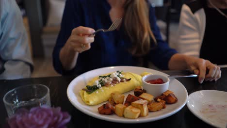 woman uses knife and fork to cut an omelet and put it into her mouth