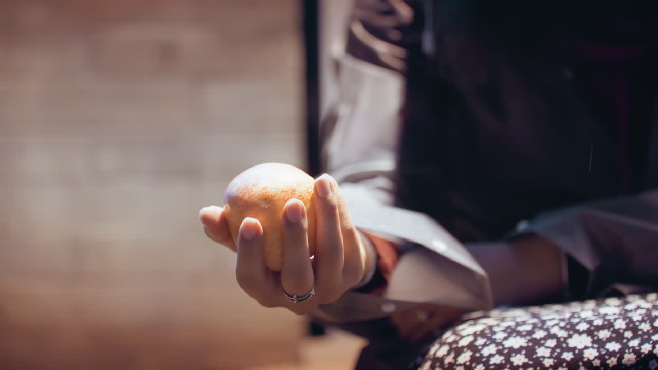 Closeup of hand clutching orange by seated commuter. Detailed view of hand grasping orange in cozy setting. Intimate shot capturing hand firmly holding orange with warm indoor lighting effects