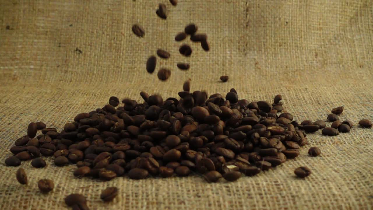 Chicchi di caffè cadono su tela di iuta al rallentatore.