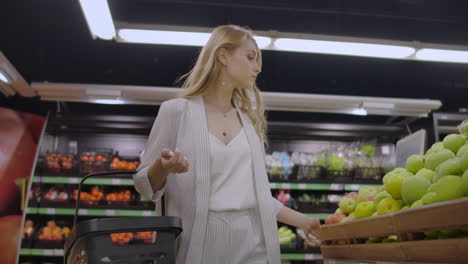 A-beautiful-woman-walks-through-the-supermarket-with-a-basket-in-her-hands-looking-at-the-shelves-of-fruit.-Buying-fresh-fruits-and-vegetables.