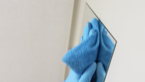 cleaning a mirror with a blue cloth and gloves