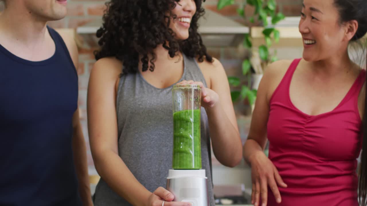 Skupina různorodých mladých lidí připravujících zelené zdravé smoothie společně doma.