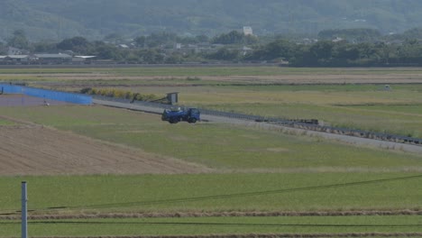 Truck-driving-on-a-rural-road-next-to-rice-paddies-with-mountains-in-the-background,-daytime