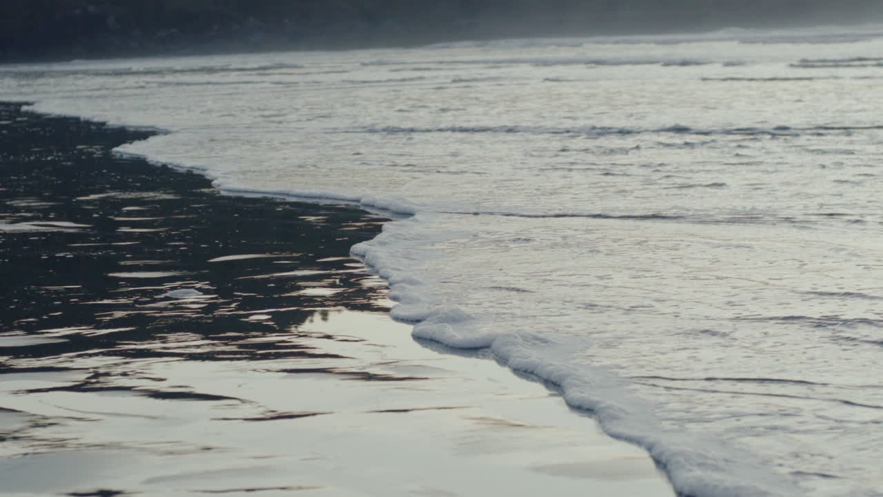 Close up of sea foam slowly moving on the wet sand with reflections