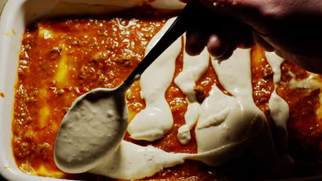 Above-view-of-lasagna-preparation,-pouring-bechamel-sauce-over-bolognese-sauce