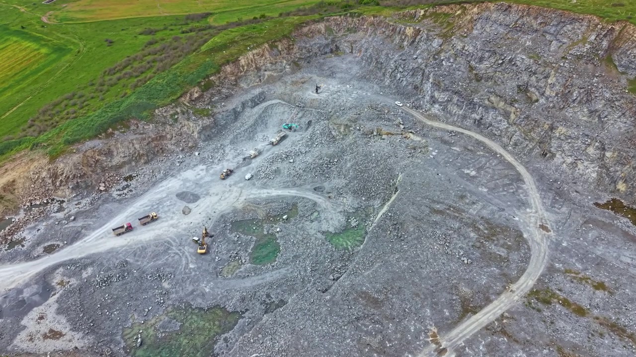 Large open-pit quarry shows heavy machinery and workers engaged in extraction process in a rural landscape