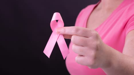Video-Des-Mittelteils-Einer-Kaukasischen-Frau,-Die-Ein-Rosafarbenes-Krebsbewusstseinsband-Hält,-Mit-Schwarzem-Hintergrund