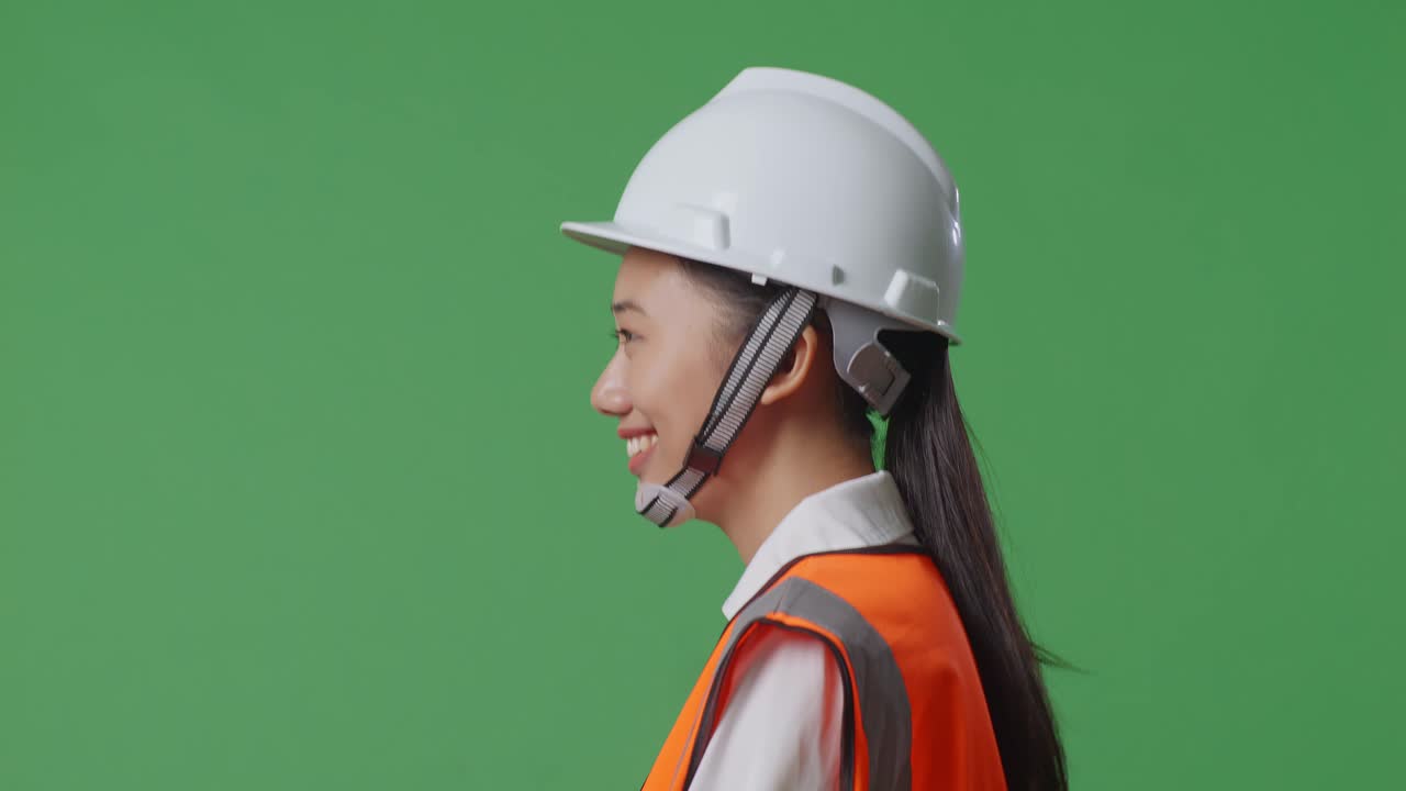 vista lateral de cerca ingeniera asiática con casco de seguridad y caminando en el estudio de fondo de la pantalla verde