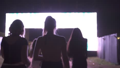 rear view following shot showing group of happy girls arriving party festival at night