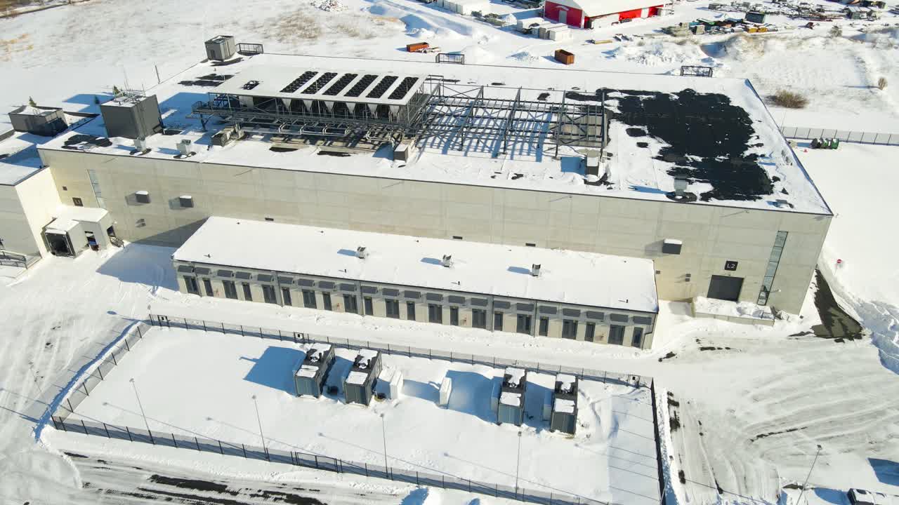 Dronekredsen om et moderne AI-datacenter, der viser køleventilatorer på taget og backup-batterilagringssystemer, der opererer under snefyldte vinterforhold i Estland.