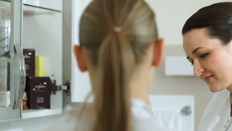 cosmetician taking cosmetic from cabinet and showing it her colleague