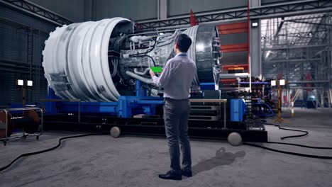 full body back view of an asian male professional worker standing with green screen smartphone with airplane engine maintenance conducted, analytics checking the turbine, industrial facility