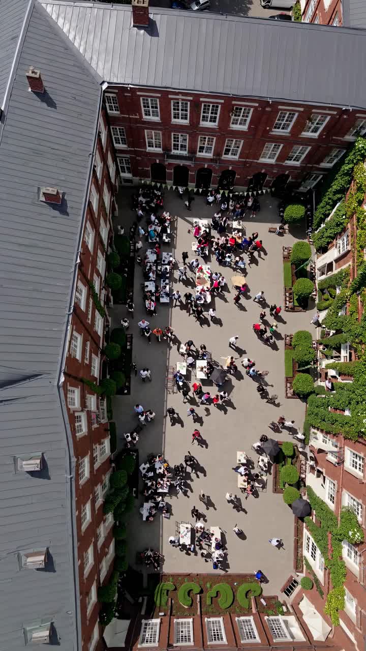 Vista aerea di un vivace cortile affollato, con persone che si mescolano e tavoli apparecchiati
