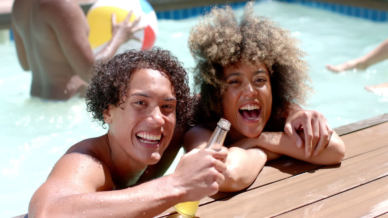 Smiling Diverse friends enjoying pool party, holding drinks and relaxing by water