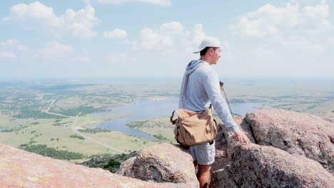 male photographer wearing camera bag taking photos with a film camera at mount scott, oklahoma facing idyllic valley