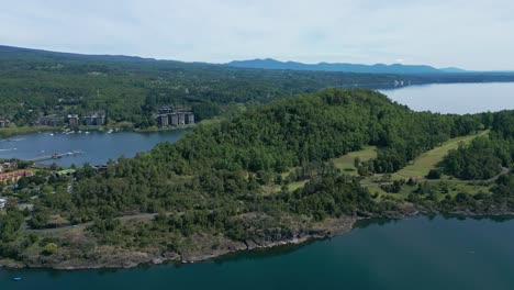 drone ascending revealing forested hill, calm lake, and modern lakeside buildings in southern chile under a clear sky