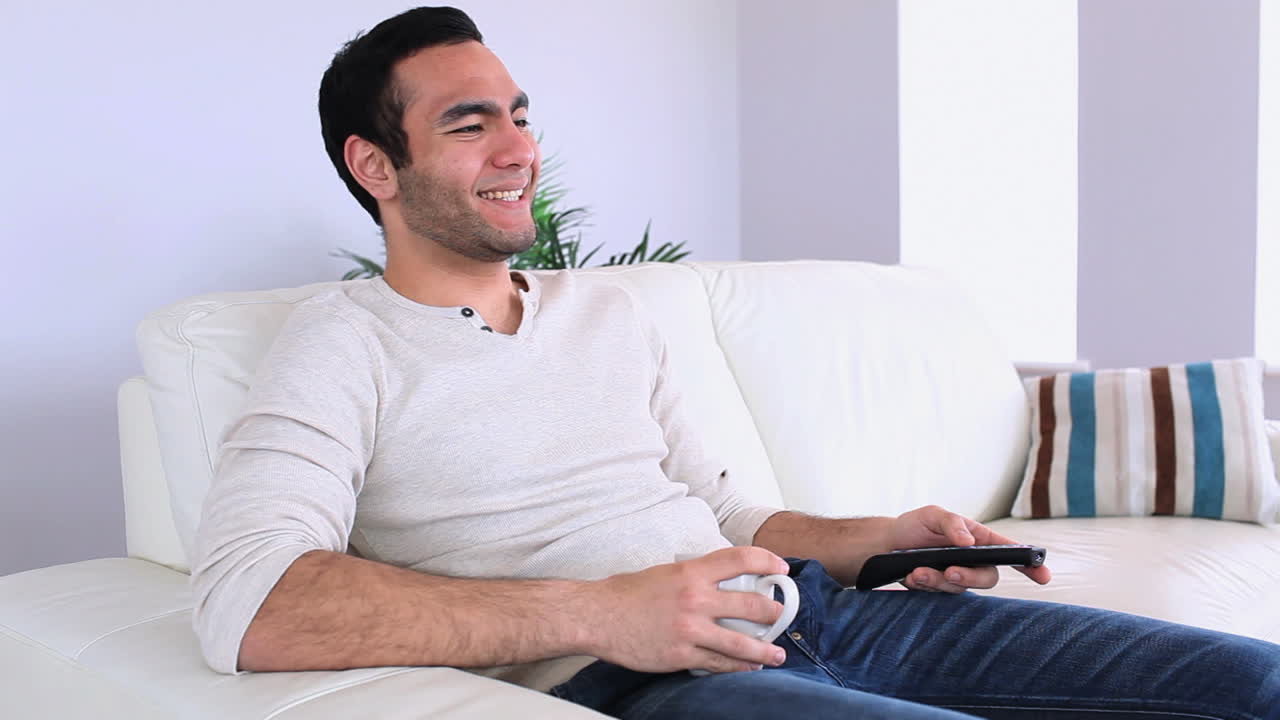 Bell'uomo che guarda la televisione rilassandosi sul suo divano
