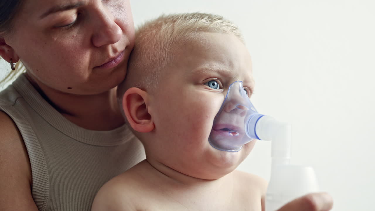 Therapeutic inhalation with a mask on the child's face. The child breathes through a nebulizer with cough medicine. Treatment of the child at home. Inhalation of the child at home