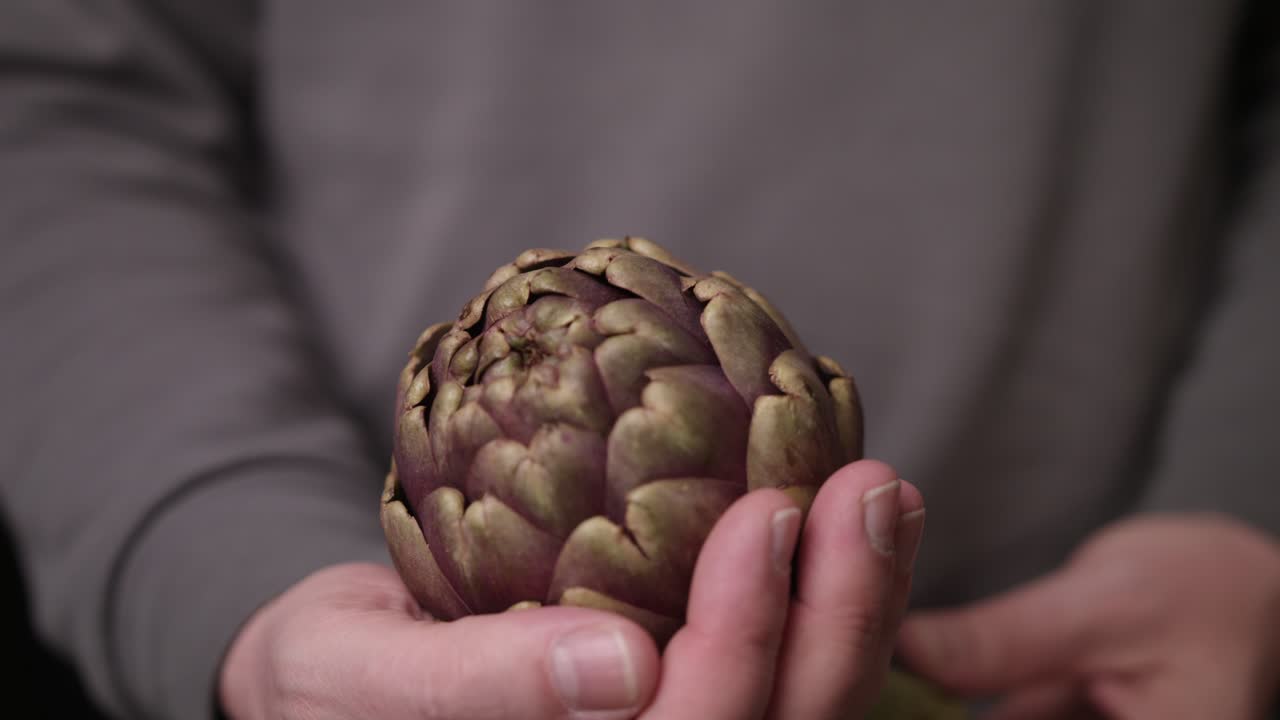 primer plano de un hombre con camiseta gris sosteniendo una hermosa alcachofa en la mano