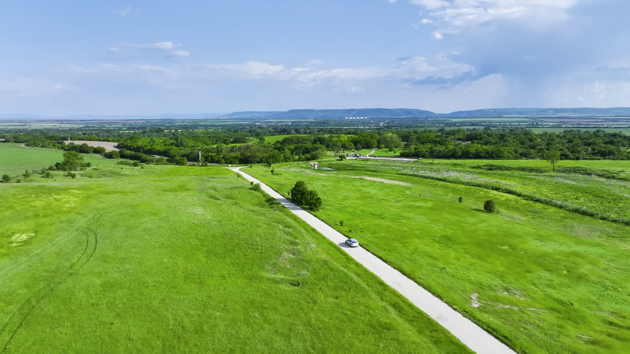 Aerial view of a car driving along a countryside road surrounded by green fields