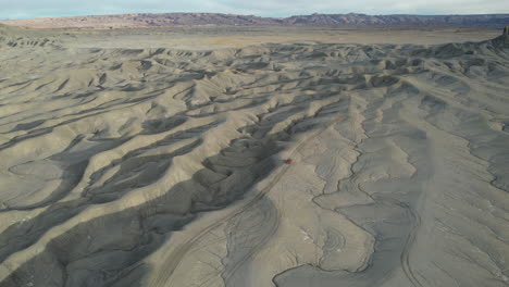 Drone-Aerial-View-of-Red-Vehicle-on-Dirtroad-and-Sandstone-Hill-in-Vastness-of-Utah-Desert-USA