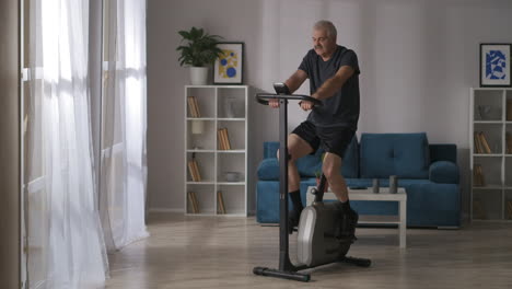 hombre sano de mediana edad está entrenando en bicicleta estacionaria en el hogar tiro general en la sala de estar fitness y estilo de vida saludable mantener en forma