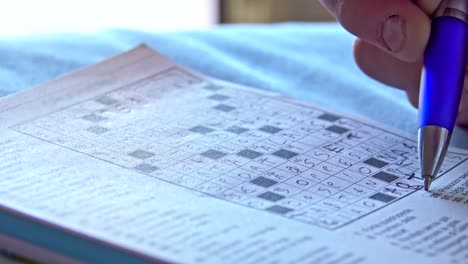 close-up of hands and pen making a crossword puzzle