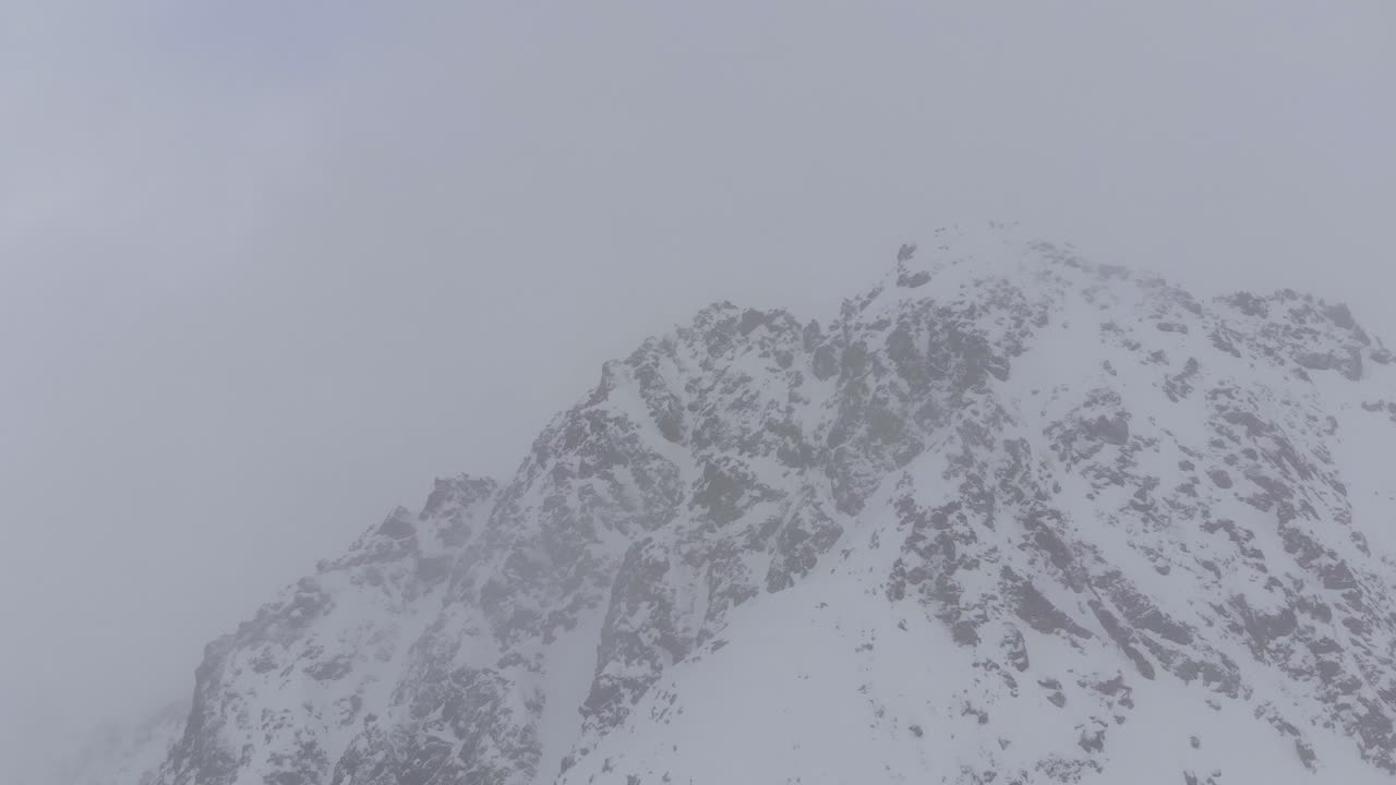 Aerial view of dramatic rocky mountains inside a blizzard storm - orbit, drone shot