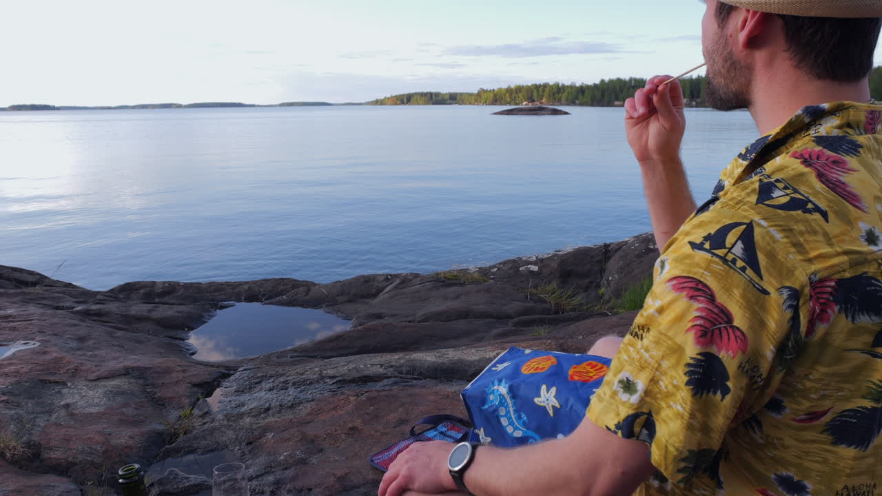 hombre en vacaciones arreglando un lago y lamiendo una barra de helado con su móvil en la mano