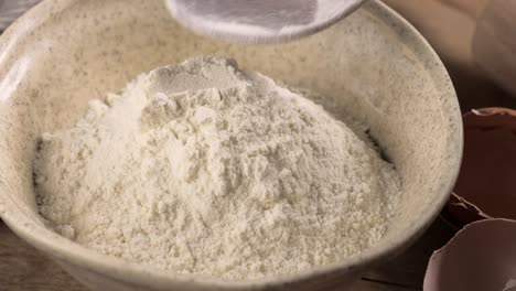 cook puts flour in a bowl with a wooden spoon for making dough