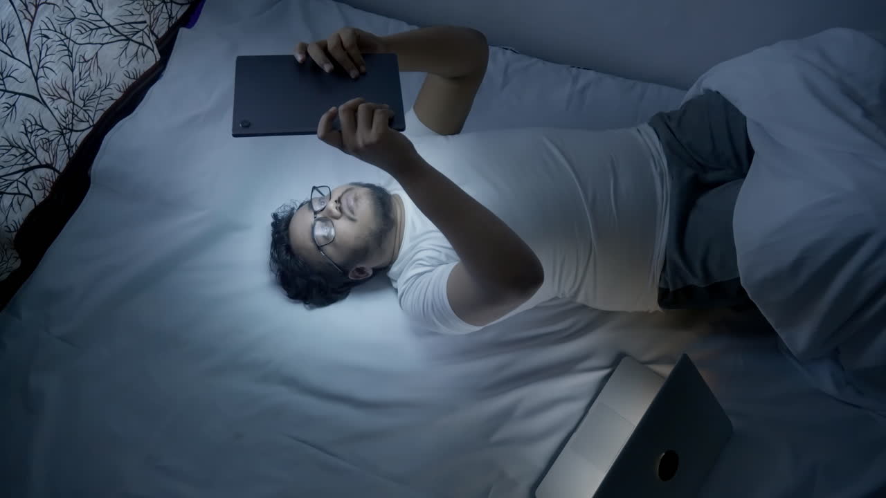 늦은 밤에 인도 남자가 소셜 미디어를 위해 디지털 태블릿을 사용합니다.