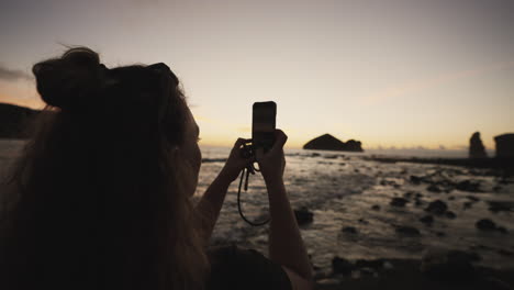 Mujer-Toma-Una-Foto-Con-El-Teléfono-Por-La-Costa-Rocosa-De-Azores-Al-Atardecer,-Primer-Plano