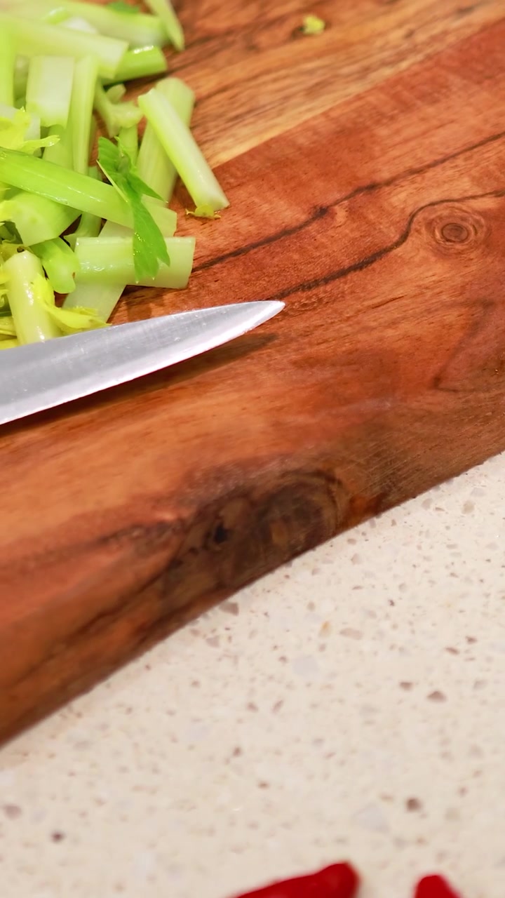 Gemüse, darunter Gurken, Schalotten und Chilis, wird auf einem Holzbrett in einer gut beleuchteten Küche geschnitten.