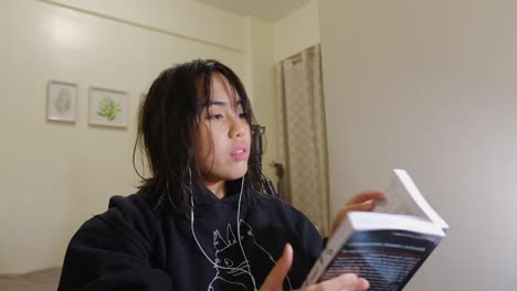 Asian, black-haired girl in a black hoodie reading different books in her bedroom