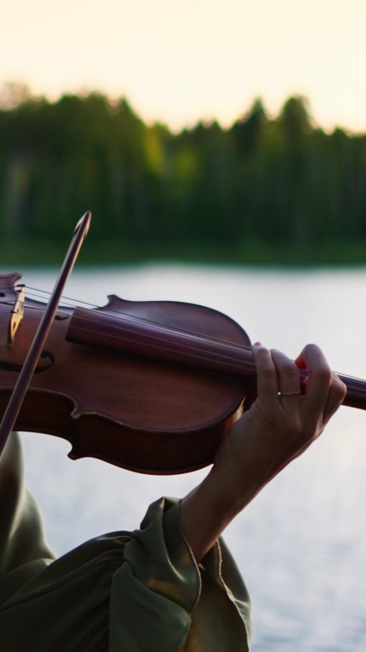 Woman Playing Violin Outdoors by a Lake at Sunset