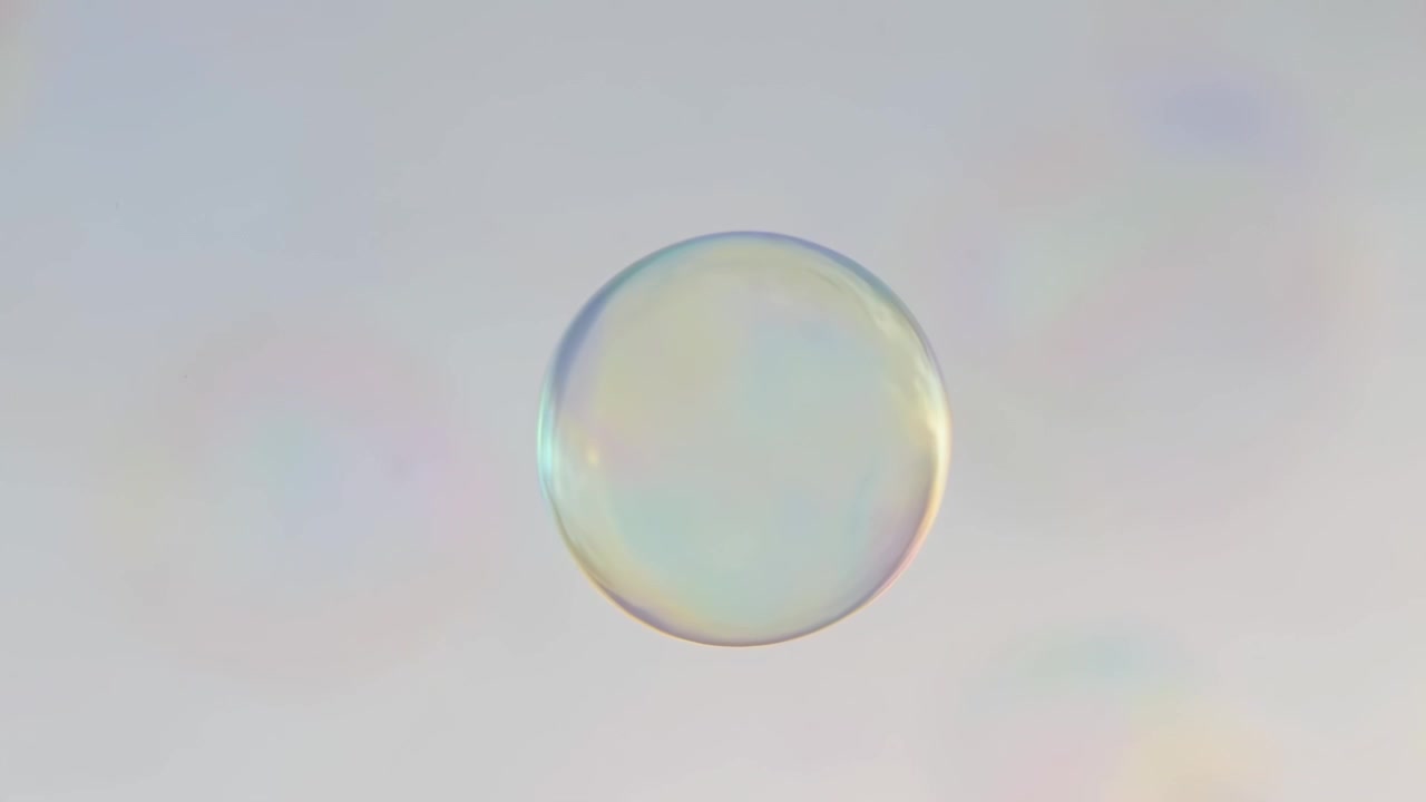 Close-up video of iridescent bubbles floating in soft light, captured from a low angle