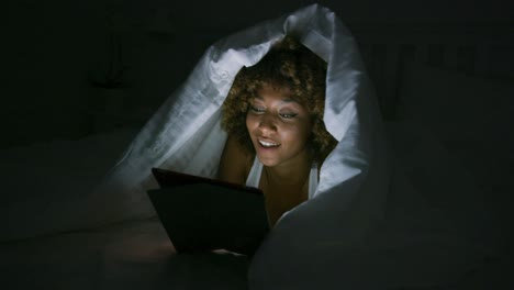 woman using tablet under blanket