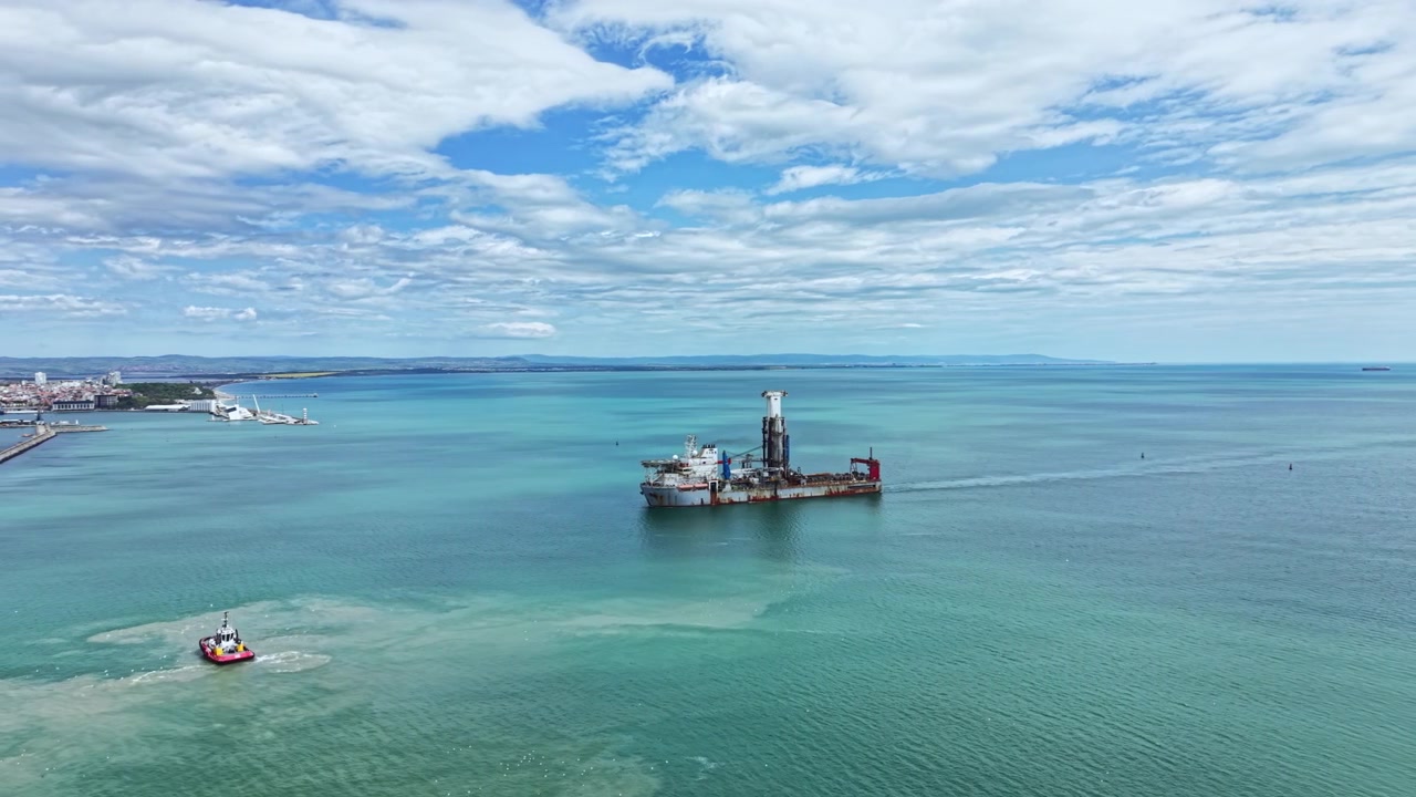 Industrial dredging vessel operates in water near coastal area with clear sky and distant land