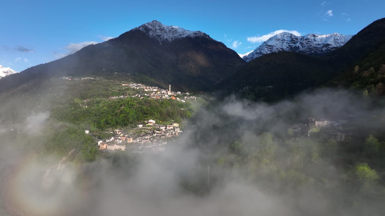 vuelo a través de las nubes con una vista panorámica de la aldea de los alpes italianos en la ladera