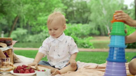 Kids-sitting-on-blanket-together-in-park.-Toddler-taking-strawberry-from-bowl