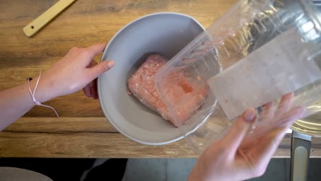 mujer vertiendo un paquete de carne picada en un bol a cámara lenta
