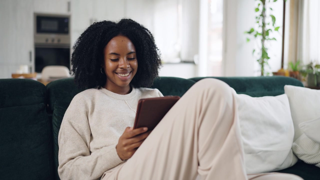 Smiling Young Woman Using Digital Tablet While Relaxing on Couch