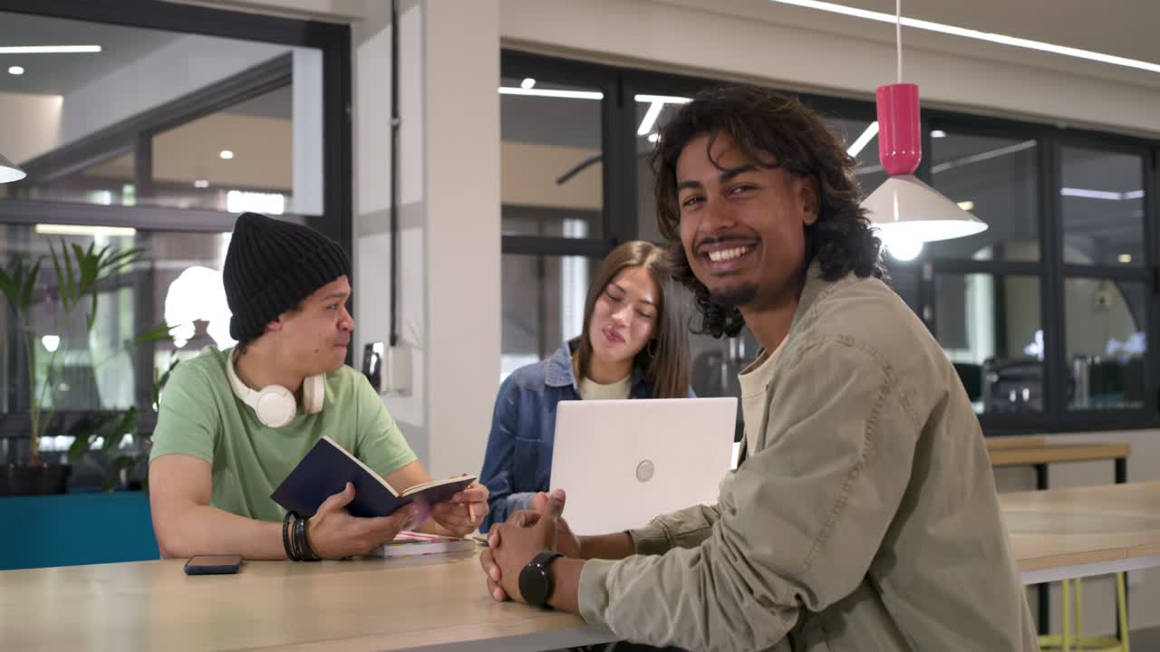 Des collègues travaillant au bureau : l'un avec un bonnet montre un carnet, celui du centre utilise un ordinateur portable, celui de droite se retourne en souriant.