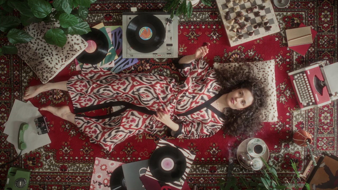 Donna in vestaglia a fantasia che si rilassa e ascolta musica in vinile su un tappeto vintage