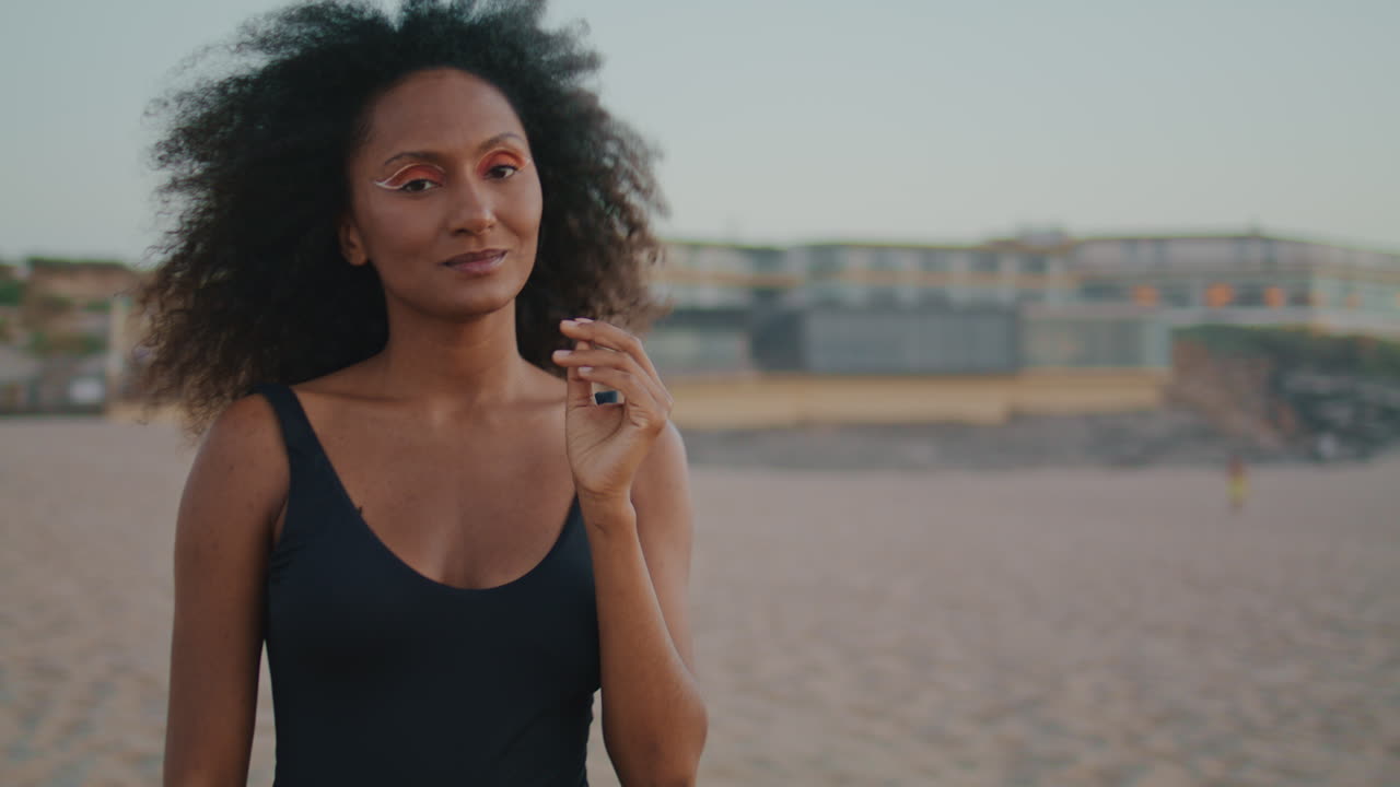 chica soñadora posando en la playa tocando el cabello rizado exuberante de cerca. mujer disfrutando de la naturaleza